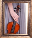 Violin in hand of a young woman seen through a frame