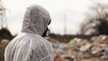 Virologist man in protective costume and respirator gas mask walking near landfill site pollution, ecological disaster