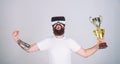 Virtual achievement concept. Guy with VR glasses won championship, hold in hand golden goblet. Man with beard in VR