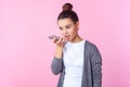 Virtual assistant. Portrait of teenage brunette girl talking to phone using digital voice app. studio shot isolated on pink