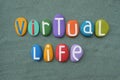 Virtual Life logo composed with multi colored stone letters over green sand