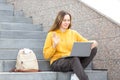 Virtual meeting. Smiling friendly caucasian woman sits on the steps of the stairs and greeting someone while