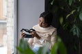 Virtual reality technology. Curious black woman holding VR headset while sitting by window Royalty Free Stock Photo