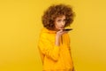 Virtual voice assistant on smartphone. Portrait of curly-haired woman in urban style hoodie giving command