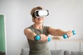 Virtual workout concept. Fit senior lady in VR glasses doing exercises with dumbbells at home