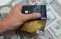 Visa bank card in a man\'s hand against the background of us dollars