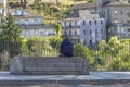 Back view of senior man relaxing sitting on a concrete and wooden bench on the pedestrian edge of a sidewalk road