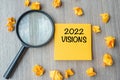 2022 VISIONS words on yellow note with crumbled paper and magnifying glass on wooden table background. New Year New Start, Idea, Royalty Free Stock Photo