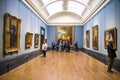 Visitors in one of the halls with hanging paintings in National Portrait Gallery, London, United Kingdom