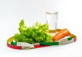 Carrot, green salad leaves and a glass of water surrounded by a measuring tape. Weight loss