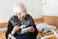 Visually impaired elderly 95 years old woman sitting at the bad trying to read with magnifying glass. Royalty Free Stock Photo