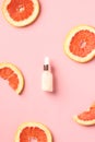 Vitamin c citrus serum dropper bottle with slices of grapefruit on pink background. Face skin care concept. Flat lay, top view