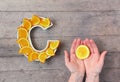 Vitamin C nutrient in food concept. Plate in shape of letter C with orange slices and woman hand with citrus on wooden background