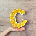 Vitamin C nutrient in food concept. Woman hand holding plate in shape of letter C with orange slices on wooden background. Flat