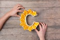 Vitamin C nutrient in food concept. Woman hands holding plate in shape of letter C with orange slices on wooden background. Flat