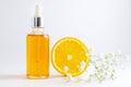 Vitamin C serum in cosmetic bottle with dropper, sliced orange and flowers on white background. Organic SPA cosmetics with herbal