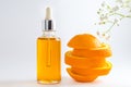 Vitamin C serum in cosmetic bottle with dropper, sliced orange and flowers on white background. Organic SPA cosmetics with herbal