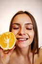 Vitamin C for skin. Delighted young pretty woman with closed eyes holding orange half over pink background Royalty Free Stock Photo