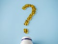 Vitamin capsules on a blue surface in the form of a question mark. Omega-3 and Vitamin D. Nutritional supplements. Yellow pills.