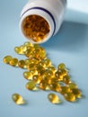 Bottle with vitamins capsules on a blue surface. Omega and vitamin D. Nutritional supplements. Opened bottle with yellow pills