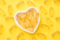 Vitamin D and Omega 3 fish oil capsules supplement in a heart-shaped plate on yellow background. Concept of healthcare