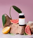 Vitamin jar on rock surrounded by grapefruit and lemon on pink background