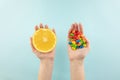 Vitamin pills and fresh orange in hands, top view. Royalty Free Stock Photo