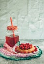 Bun with fresh raspberries on a white plate and red stewed fruit in a glass jar; summer light breakfast for a good mood