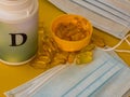 Vitamine D capsules near plastic conainer and  medical face masks on bright yellow table Royalty Free Stock Photo