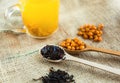 Vitaminic healthy black tea with sea buckthorn in red cup with fresh raw sea buckthorn berries and black tea in wooden spoons Royalty Free Stock Photo