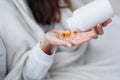 Vitamins and food supplements concept. Female hand pouring yellow pills out of bottle into palm. Woman spilling out