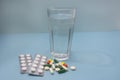 Vitamins and pills on blue background. Glass of water for taking medicine. Side view, close-up, selective focus