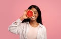 Pretty African American woman covering eye with grapefruit half on pink studio background Royalty Free Stock Photo
