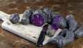 Vitelotte, french purple potatoes sliced in half with a knife on wooden board at rustic kitchen table. Blue variety of popular pot Royalty Free Stock Photo