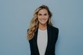 Vivacious blond woman in stylish blazer with happy beaming smile standing with hands behind her back