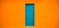 Vivid bright orange colour facade with blue-green closed door in the center of large empty orange wide wall texture background