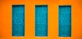 Vivid bright orange wall house facade with three blue-green closed doors on large empty orange wide wall texture background