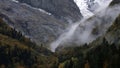 Vivid clouds on rocky snowy mountain slope. Creative. Colorful trees at the foot of mountains. Royalty Free Stock Photo