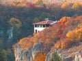 Vivid colourful yellow red orange autumn fall season. Small cottage house in mountains on the rocks surrounded by trees.