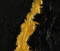 Vivid contrast of black and gold abstract background of metallic gold paint swirling over charred black ashes