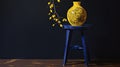 Vivid Contrasts: Lush Lemon Tree in a Sunny Yellow Pot with a Blue Stool Against a Dark Wall. Royalty Free Stock Photo