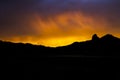 Vivid Sunset Over Black Mountain Ridgeline Silhouette Through Rain in Desert Royalty Free Stock Photo