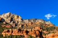 Vividly colored, rocky hillside in Sedona, Arizona. Right red sandstone with deep blue sky and white cloud in background.