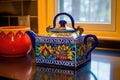 a vividly painted, mexican talavera teapot on a brightly tiled countertop