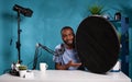 Vlogger explaining features of studio flash light modifier sitting at desk with microphone