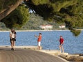 Promenade with pine trees by the sea and people walking and riding on electric scooter