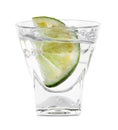 Vodka splashing out of shot glass with lime on white background Royalty Free Stock Photo