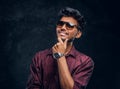 Vogue, fashion, style. Cheerful young Indian guy wearing a stylish shirt and sunglasses posing with hand on chin. Royalty Free Stock Photo