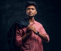 Vogue, fashion, style. Handsome young Indian guy wearing a pink shirt holding a jacket on his shoulder and looking Royalty Free Stock Photo