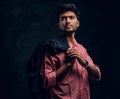 Vogue, fashion, style. Handsome young Indian guy wearing a pink shirt holding a jacket on his shoulder and looking Royalty Free Stock Photo